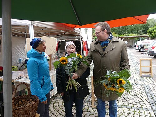 Bürgermeister Dr. Benedikt Grünewald überreicht Maria Scheidler und ihrer Tochter Marion Englbrecht ein kleines Dankeschön für die jahrelange Treue zum Wochenmarkt.
