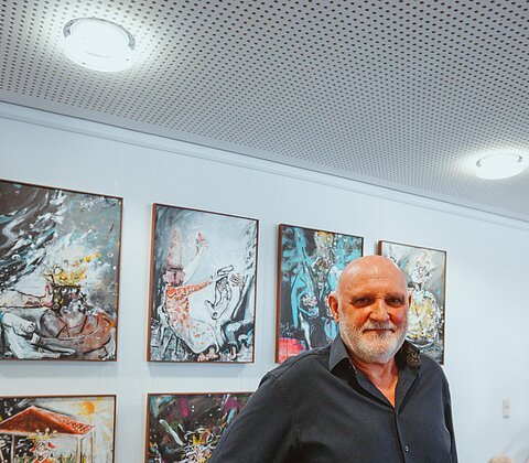 Künstler Uli Koch steht vor einem Teil seiner Ausstellung – stolz, glücklich und ganz im Einklang mit seinen Werken, die Geschichten erzählen und zum Verweilen einladen.