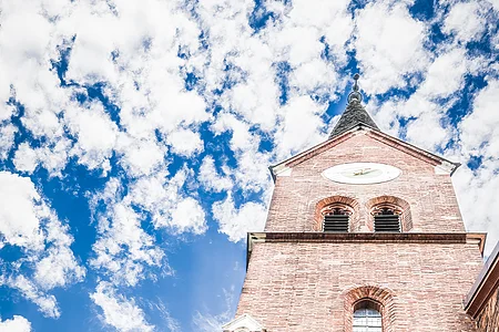 Zwei Wanderer werden von unten fotografiert wie sie hinauf auf den Kirchturm aus roten Ziegeln der Kirche St. Nikolaus blicken.