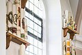 Zu sehen sind Wandregale um ein Fenster herum auf welchen die ehemaligen Osterkerzen stehen.