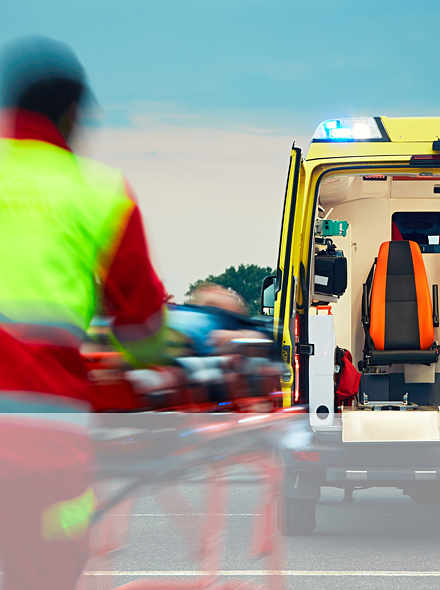 Ein Rettungssanitäter fährt eine Person auf einer rollbaren Trage in Richtung eines offenen Rettungswagens.