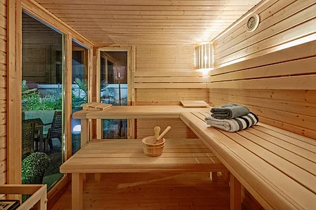 Innenraum einer Holzsauna mit Bänken, einem Eimer und Handtüchern, Fenster mit Blick auf Garten.