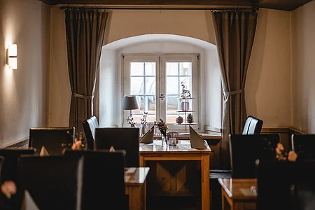 Essbereich mit Tisch und Stühlen vor einem Fenster mit Vorhängen, dekoriert mit Lampe und Figuren.