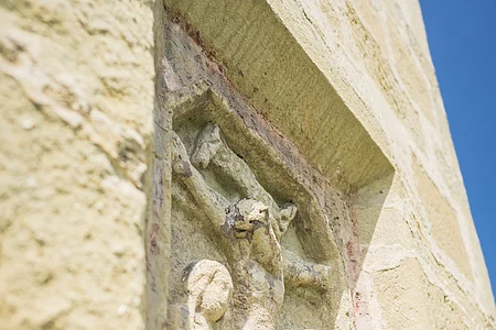 Steinrelief an einer Wand, zeigt drei stehende Figuren unter einem Kreuz.