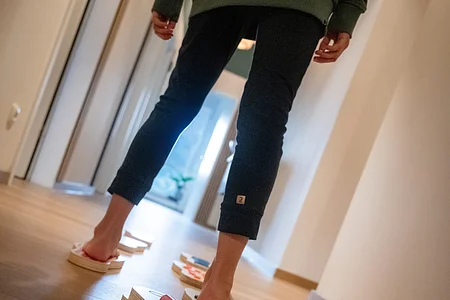 Person balanciert auf einem Holzbrett in einem Flur, mehrere Balancebretter liegen auf dem Boden.