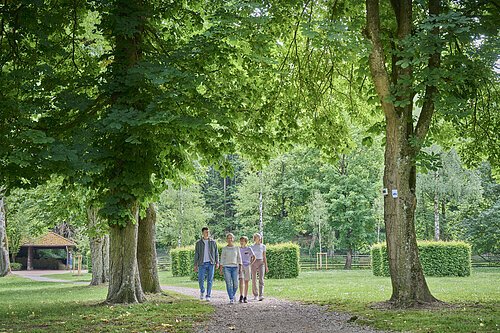 Familienspaziergang im Kurpark eine Mutter spaziert mit ihren drei Kindern durch den Bad Abbacher Kurpark unter Bäumen hindurch.