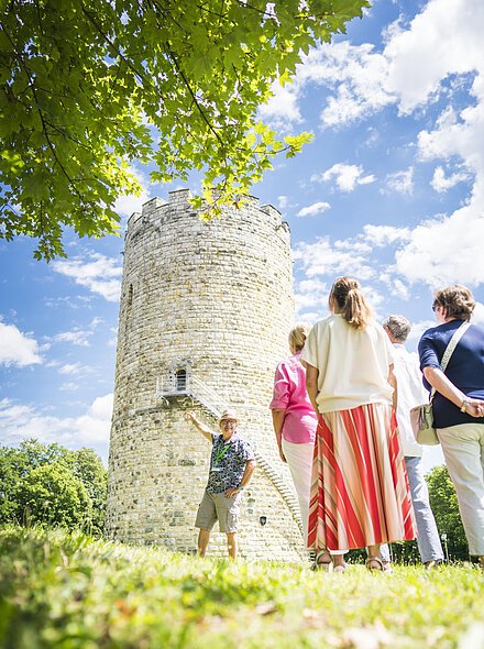 Gruppe von Menschen vor einem runden Steinturm, ein Mann zeigt auf den Turm.