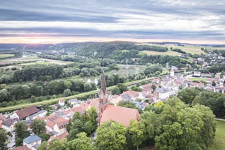 Bad Abbach und Blick ins Donautal Luftaufnahme einer Stadt mit Kirche, umgeben von Bäumen, Fluss und Hügeln im Hintergrund.