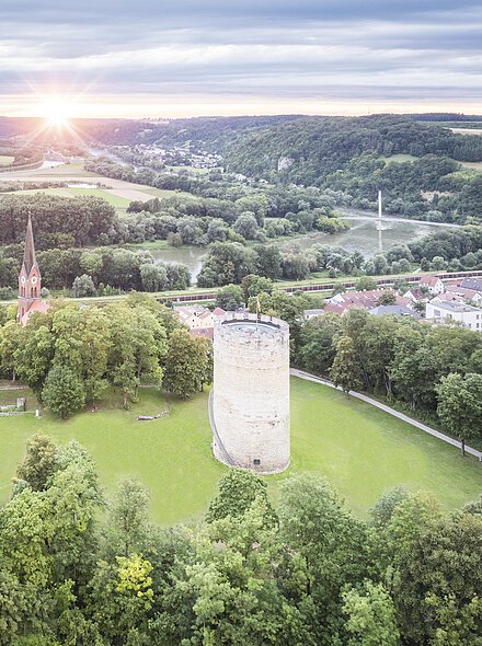 Bad Abbach Burgberg Vogelperspektive Luftaufnahme einer Landschaft mit einem runden Turm und einer Kirche mit spitzem Turm, umgeben von Bäumen und Wiesen.