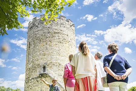 Gruppe von Menschen steht vor einem alten Steinturm, ein Mann zeigt auf den Turm.