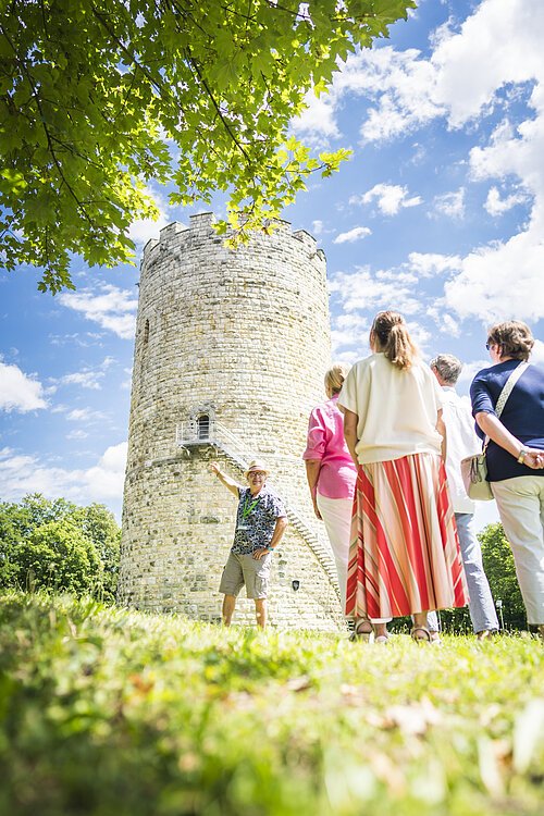 Gästeführung Heinrichsturm Gruppe von Menschen vor einem runden Steinturm, ein Mann zeigt auf den Turm.