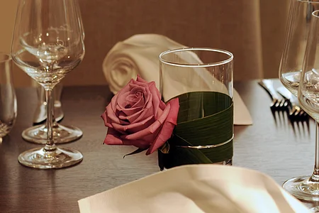 Gedeckter Tisch mit Weingläsern, Serviette und Glas mit rosa Rose in einem Restaurant.