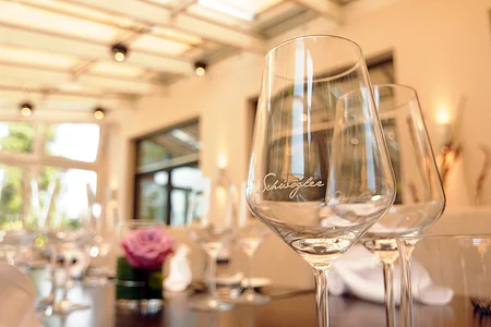 Weingläser auf einem gedeckten Tisch in einem hellen Raum mit großen Fenstern und Blumenarrangement.