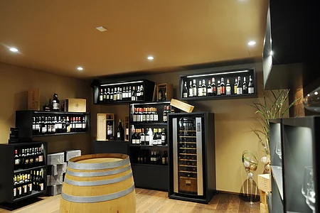 Weinkeller mit Regalen voller Weinflaschen, einem Weinkühlschrank und einem Holzfass in der Mitte.