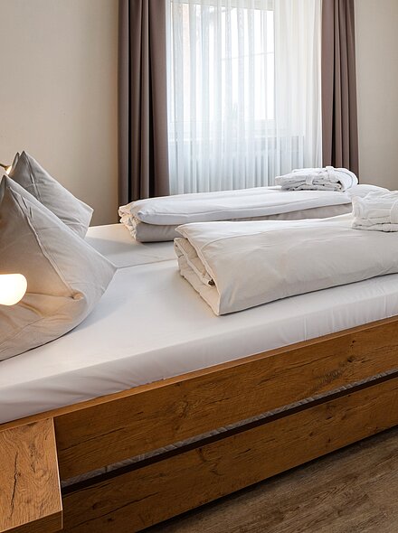 Hotelzimmer mit einem Doppelbett, zwei Sesseln, einem kleinen Holztisch und einem an der Wand montierten Fernseher.