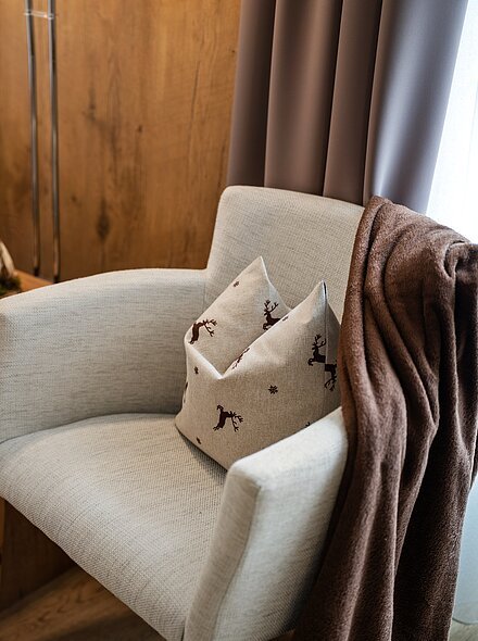 Hotel Gasthof Zur Post Zwei gepolsterte Stühle mit Hirschkissen, ein Holztisch dazwischen, darauf ein Buch und eine Dekoration.