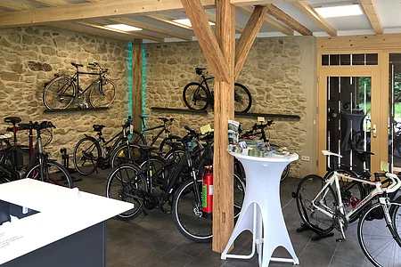 Fahrradladen mit mehreren Fahrrädern, Holzbalken, Steintapete und einem weißen Stehtisch mit Broschüren.