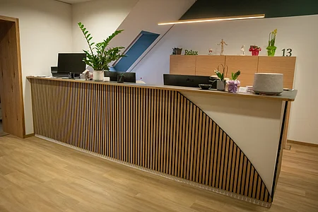 Empfangstresen mit Holzlamellen, Pflanzen und Monitoren in einem modernen Büro mit Holzboden.