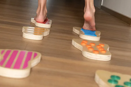 Füße laufen barfuß über bunte Holzplatten mit verschiedenen Mustern auf einem Holzboden.