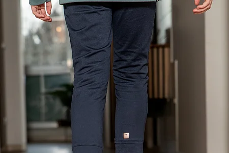 Person balanciert barfuß auf einem Holzspielzeug mit bunten Elementen auf einem Holzboden.