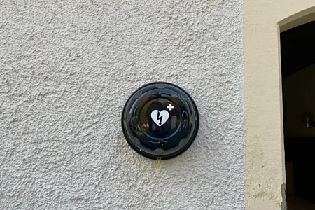 Wandmontiertes schwarzes Gehäuse mit Herzsymbol und Blitz für automatisierten externen Defibrillator.