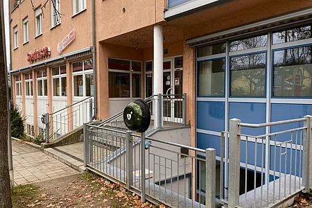 Eingang eines Sparkassen-Gebäudes mit Treppe, Rampe und einem Defibrillator an einem Geländer.