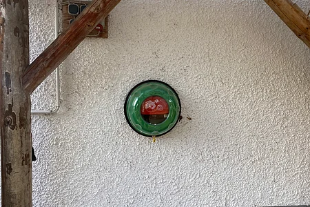 Grüne runde Wandhalterung mit rotem Defibrillator an weißer rauer Wand unter Holzbalken.
