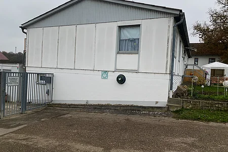 Seitenansicht eines weißen Gebäudes mit einem Fenster, einem Tor und einem Defibrillator an der Wand.