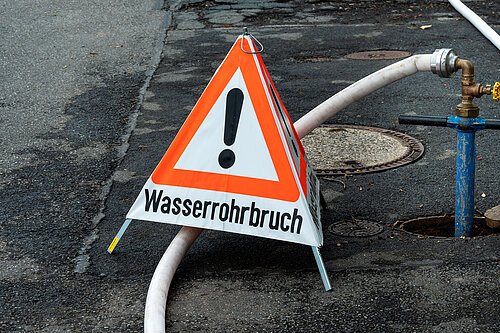 Warndreieck Wasserrohrbruch Warndreieck (Warnpyramide) mit dreiseitigen Warnhinweis WASSERROHRBRUCH und dem Warnsymbol Gefahrenstelle, welches aus einem roten Dreieck und einem schwarzen Ausrufezeichen besteht.