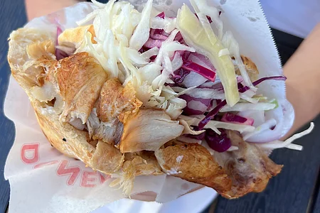 Hand hält gefülltes Fladenbrot mit gegrilltem Hähnchen und Krautsalat in Papierverpackung.