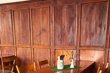 Holztisch mit vier Stühlen und Tischdeko vor einer Holzvertäfelung in einem Raum mit Fliesenboden.