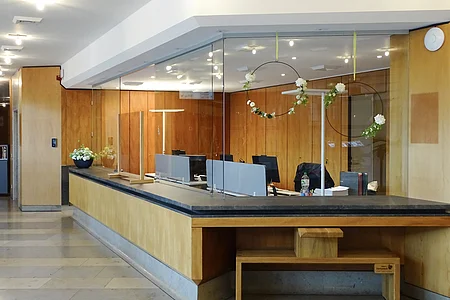 Empfangstresen mit Glasabtrennung und Holzverkleidung in einem Büro mit Blumenarrangements.
