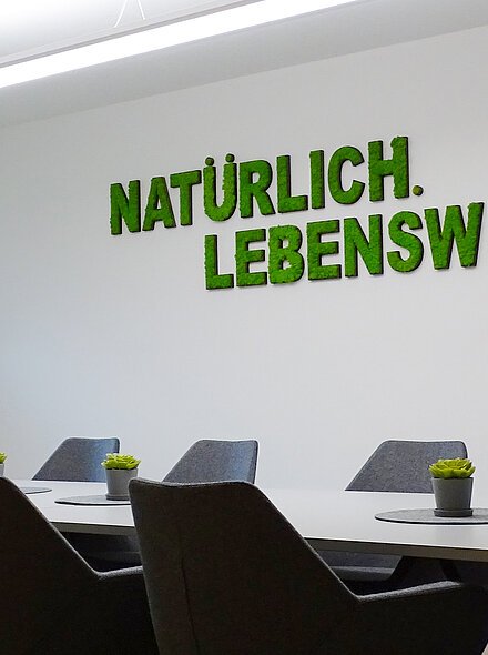 Besprechungsraum im Kurhaus Konferenzraum mit Tisch, acht Stühlen, Uhr, Fenster, Whiteboard und Schriftzug „Natürlich. Lebenswert“ an der Wand.