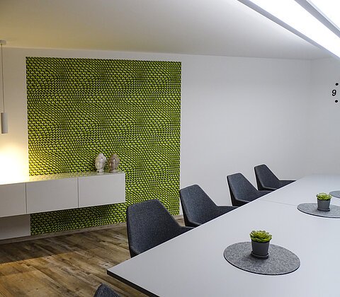 Konferenzraum mit langem weißen Tisch, grauen Stühlen, grüner Wandgestaltung und zwei Buddha-Kopf-Dekorationen.