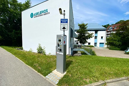 Parkautomat vor weißem Gebäude mit Aufschrift Asklepios Klinikum Bad Abbach bei sonnigem Himmel