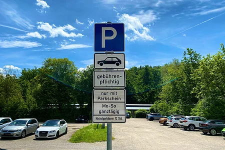 Parkplatzschild mit Hinweis auf gebührenpflichtiges Parken nur mit Parkschein, Höchstparkdauer 12 Stunden, umgeben von geparkten Autos.