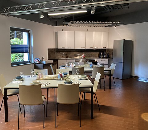 Moderne Küche mit zwei gedeckten Tischen, weißen Stühlen, weißen Schränken und grauem Kühlschrank.