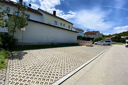 Parkplatz mit Gittersteinen vor Wohnhäusern und blauem Himmel mit Wolken an einem sonnigen Tag