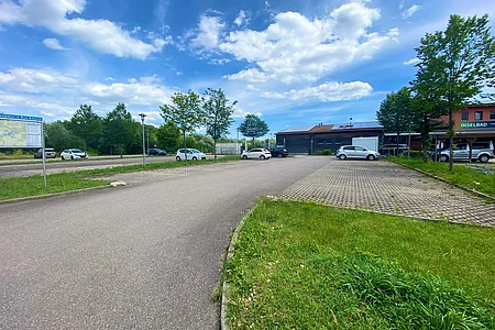 Parkplatz mit mehreren Autos, Bäumen und einem Gebäude mit dem Schild „Inselbad“ unter blauem Himmel mit Wolken