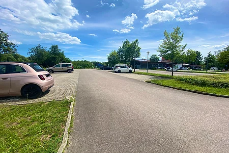 Parkplatz mit mehreren geparkten Autos, Bäumen und blauem Himmel mit Wolken bei Tageslicht