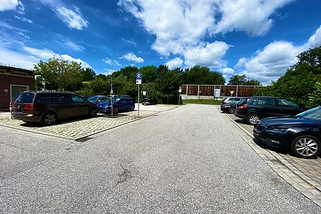 Parkplatz mit mehreren geparkten Autos, Bäumen und blauem Himmel mit Wolken im Hintergrund