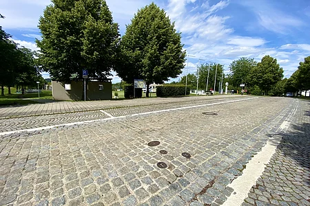 Pflasterstraße mit Parkplätzen, Bäumen und blauem Himmel mit Wolken an einem sonnigen Tag