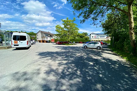 Parkplatz mit mehreren geparkten Autos, Bäumen und Gebäuden unter blauem Himmel mit Wolken