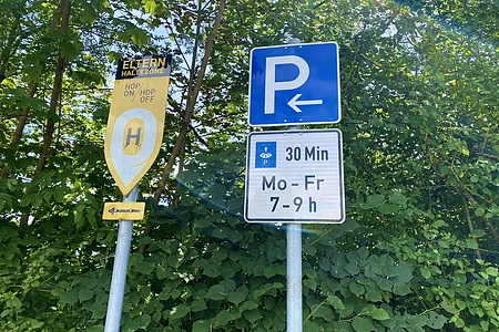 Verkehrsschilder für Elternhaltezone und 30-Minuten-Parkzeit von Montag bis Freitag 7-9 Uhr, umgeben von Bäumen.