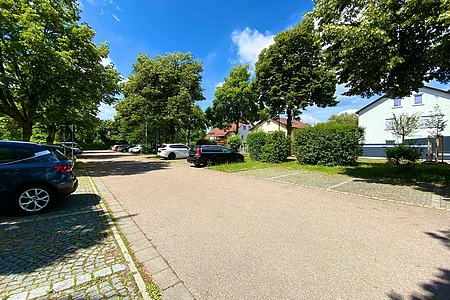 Parkplatz mit mehreren Autos, Bäumen und Wohnhäusern unter blauem Himmel an einem sonnigen Tag