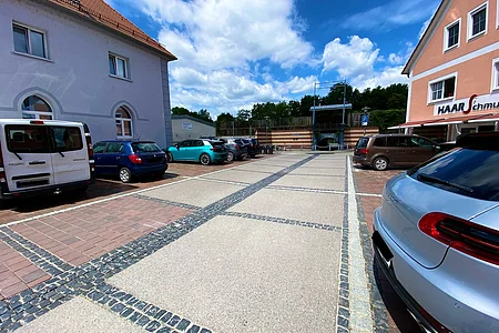 Parkplatz mit mehreren geparkten Autos zwischen zwei Gebäuden unter blauem Himmel mit Wolken