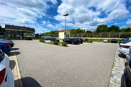 Parkplatz mit mehreren geparkten Autos, solarbetriebenes Gebäude und bewölkter Himmel im Hintergrund