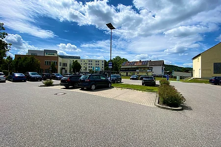 Parkplatz mit mehreren Autos vor einem Gebäude mit Solarpanelen auf dem Dach unter bewölktem Himmel