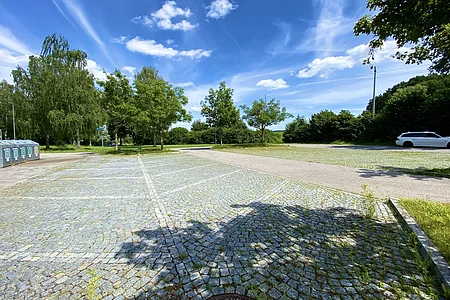 Leerer gepflasterter Parkplatz mit Bäumen und blauem Himmel mit Wolken im Hintergrund.