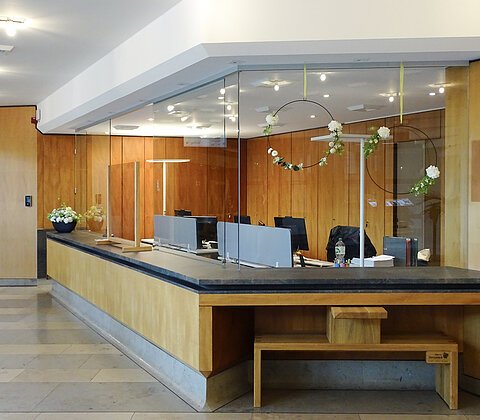 Empfangstresen mit Glasabtrennung und Holzverkleidung in einem Büro mit Blumenarrangements.